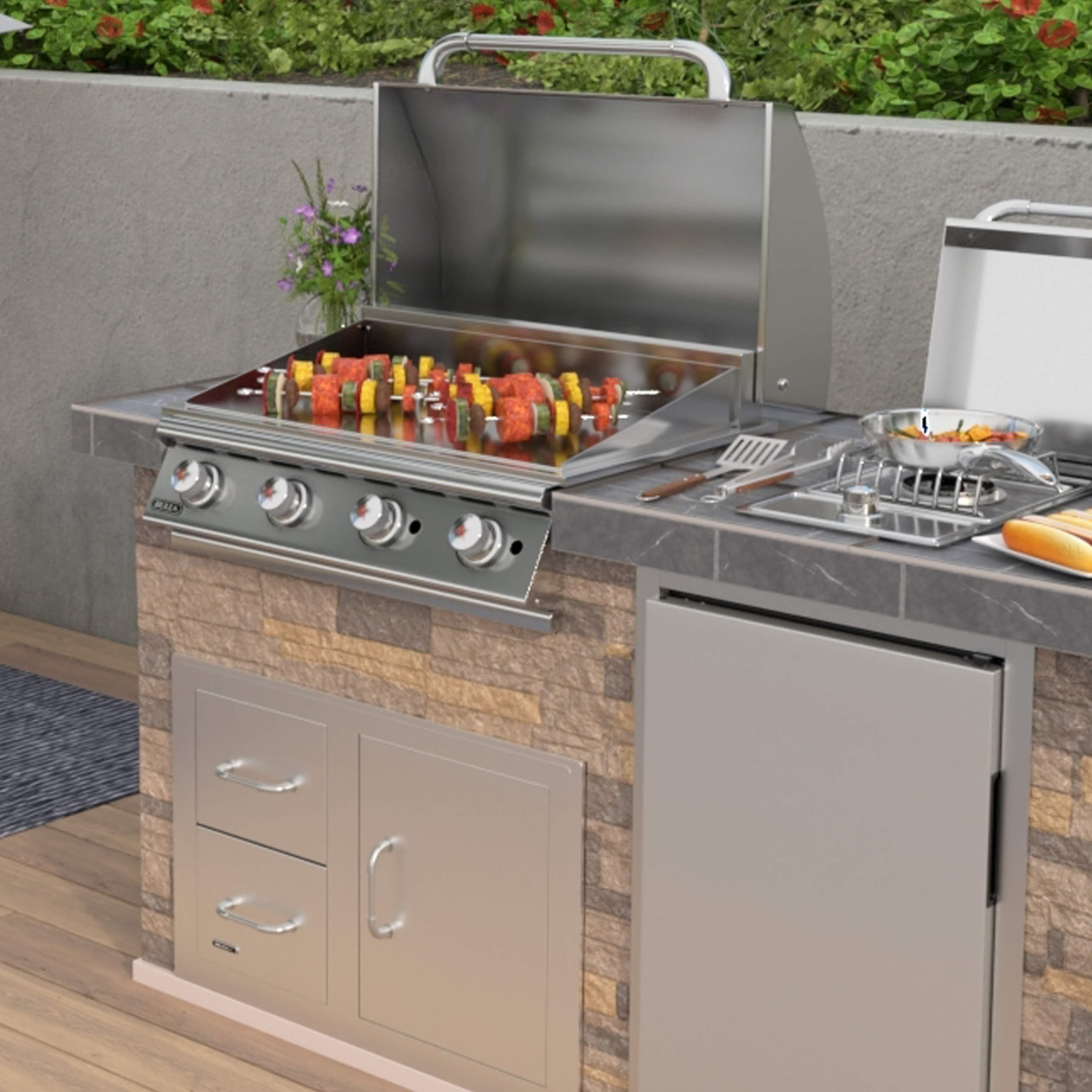 Bull BBQ 30-inch four-burner built-in flat top griddle mid-cook with vegetable kebabs on the chrome surface, hood propped, side burner running — stacked-stone outdoor kitchen island with matched Bull storage.