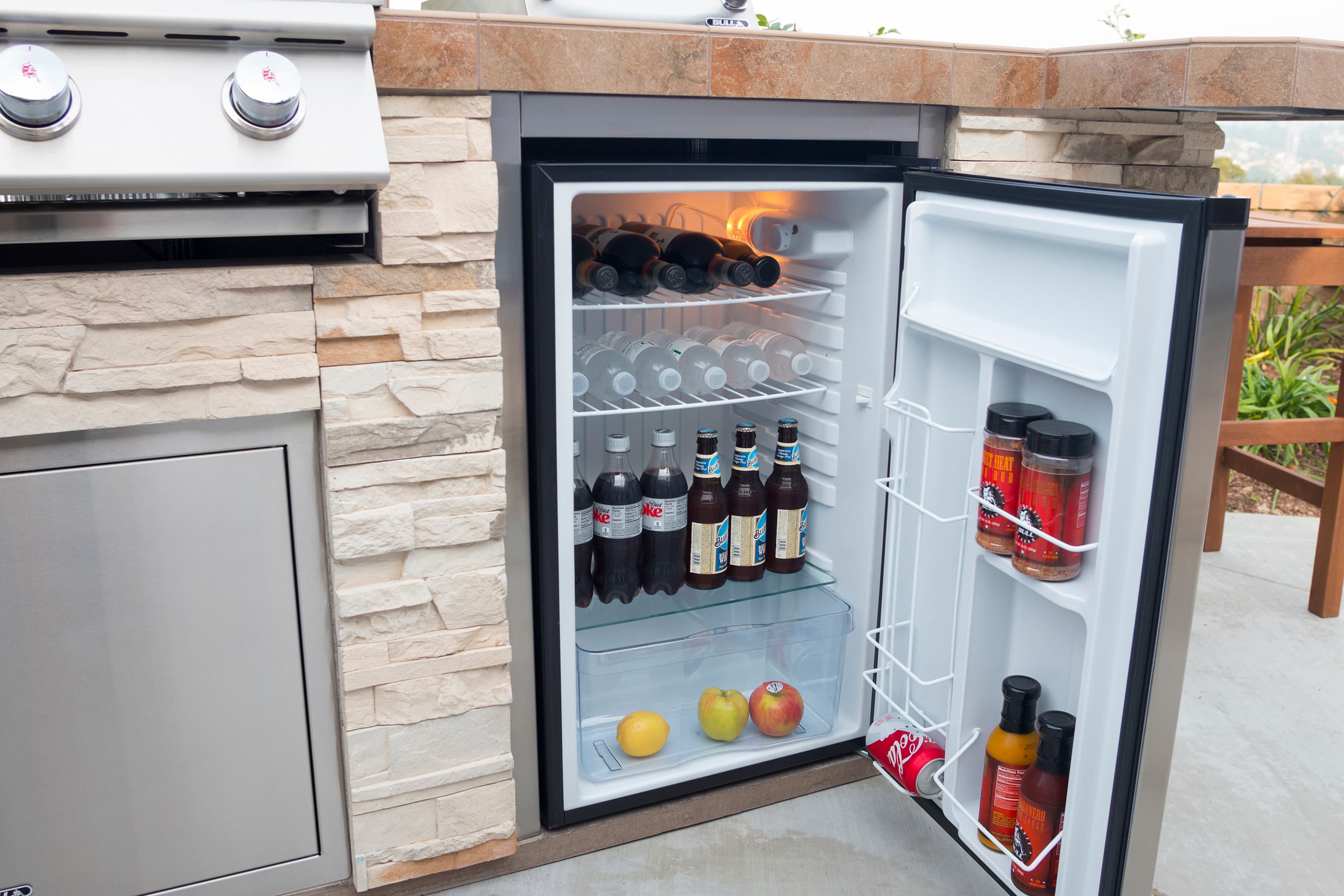 Stainless steel canopy vent hood installed above a built-in grill under a covered patio, with visible ductwork rising into the ceiling.