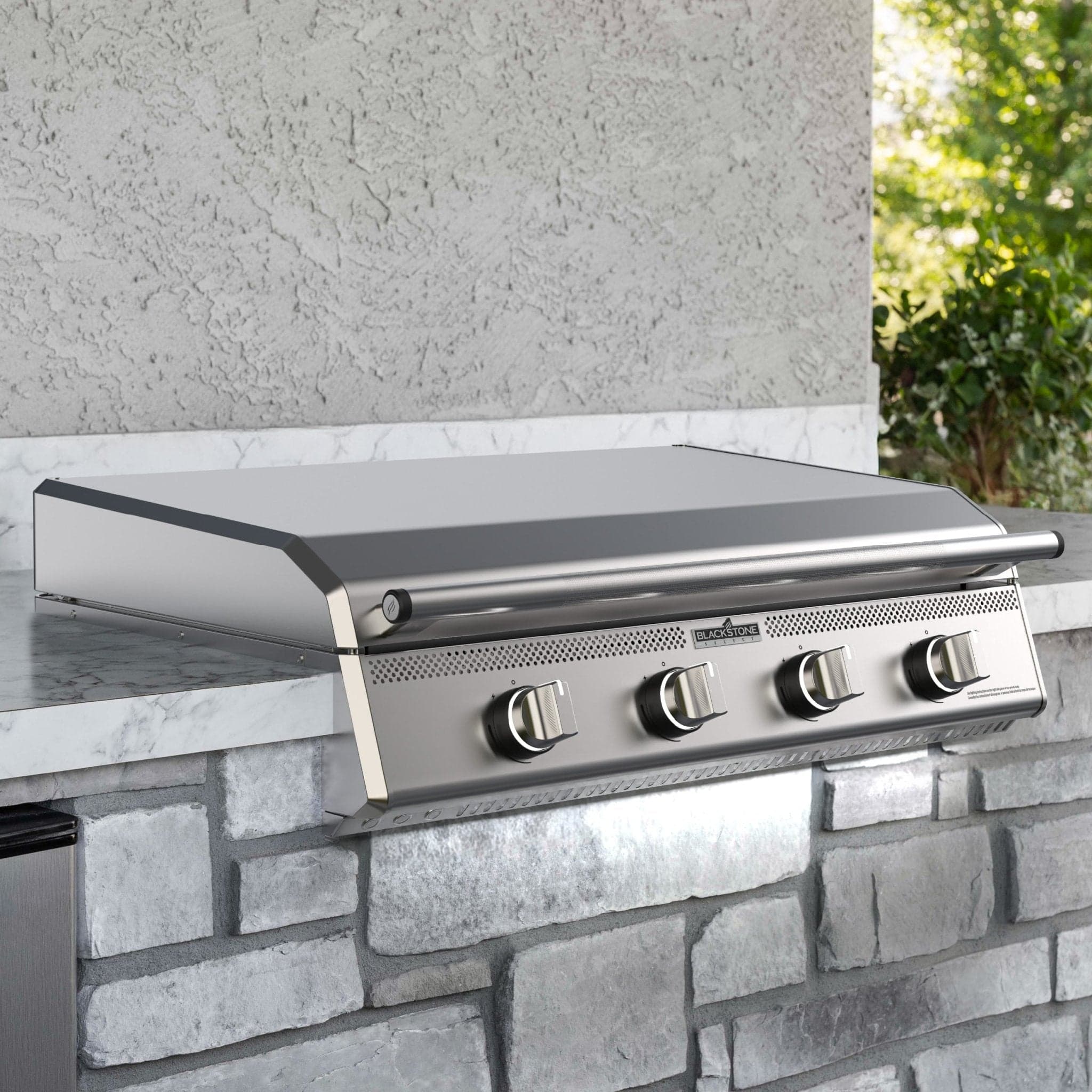 Blackstone 36-inch Select Series built-in griddle head installed in a stone and marble outdoor-kitchen island with greenery backdrop.