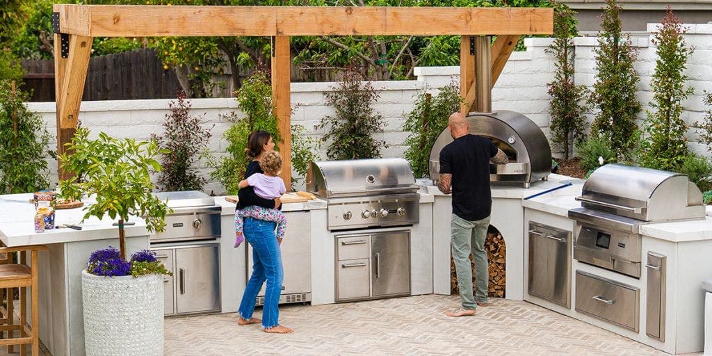 Coyote CL Series 4-burner built-in gas grill in polished 304 stainless with hood open, mounted into a stone outdoor kitchen chase.
