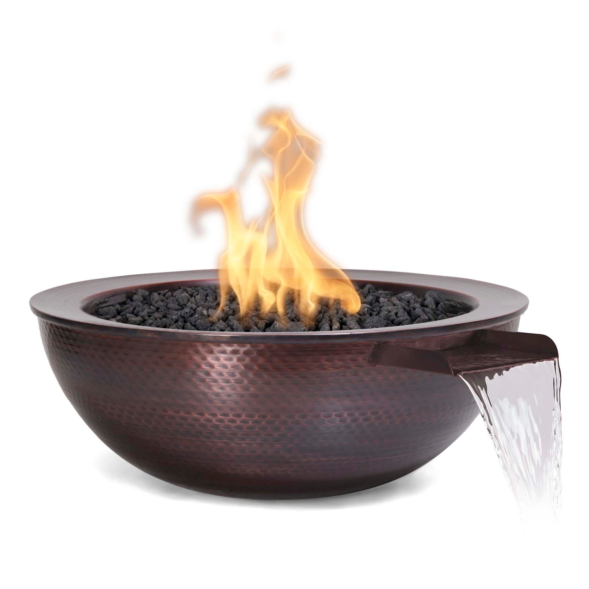 The Outdoor Plus Sedona 27-inch hammered copper fire and water bowl with a clean tall flame burning over black lava rock — the electronic-ignition variant mid-cycle, flame fully developed after a 5-second button press.